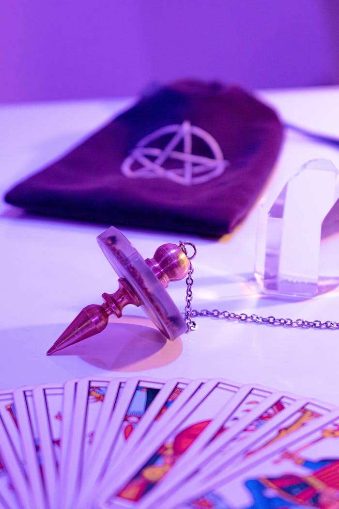 A mystical setup featuring tarot cards, a pendulum, and a velvet bag under pink lighting.