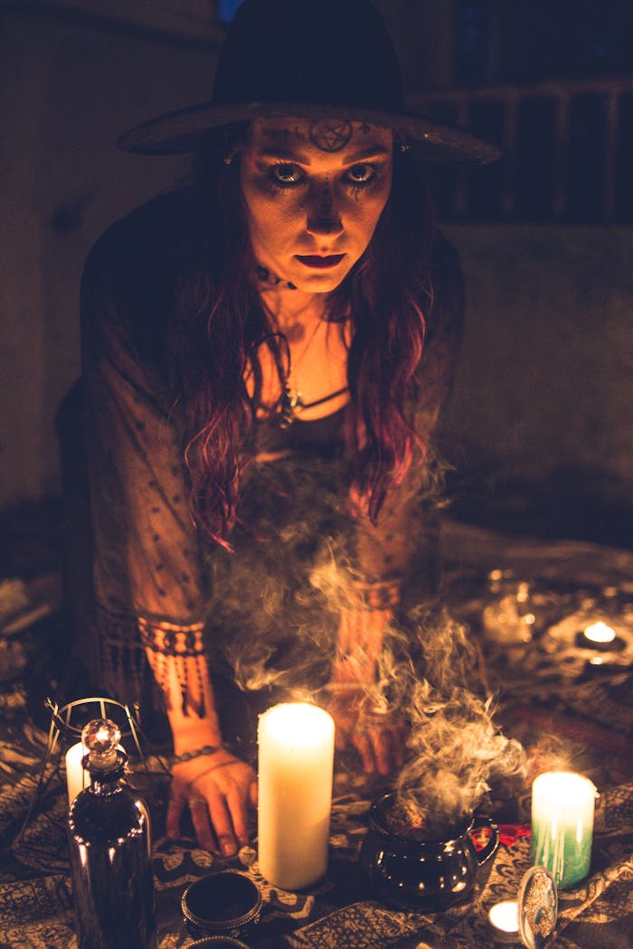 Mysterious woman conducts a mystical ritual with candles and smoke in a dark, atmospheric setting.